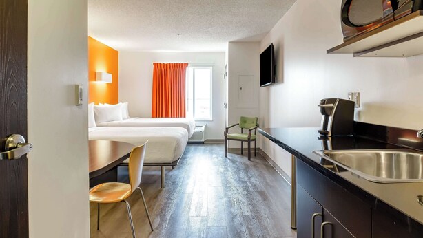 A compact hotel room with a bed, a desk, a chair, a kitchenette, and a TV. - Motel 6 Headingley, MB - Winnipeg West (Headingley)