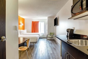 Une chambre d’hôtel de taille réduite, comprenant un lit, un bureau, une chaise, une kitchenette et un téléviseur.