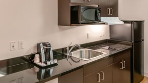 A modern kitchen with a black countertop, stainless steel sink, and a built-in microwave. - Motel 6 Headingley, MB - Winnipeg West (Headingley)