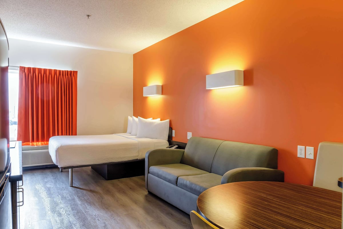 A hotel room with a bed, a sofa, a wooden table, and two wall-mounted light fixtures.