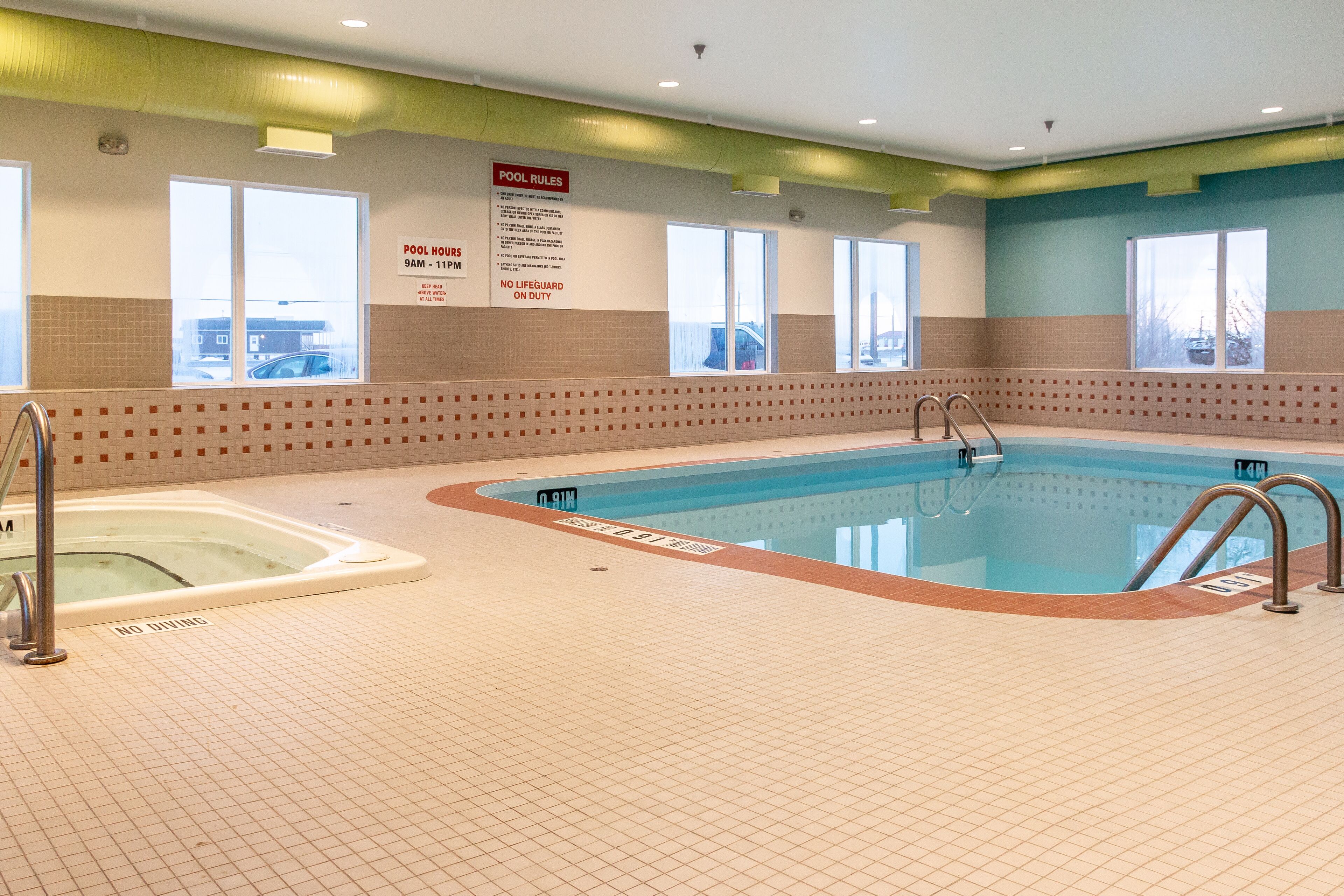 Une piscine intérieure où les règles d’utilisation sont clairement affichées sur le mur, avec un poste de surveillance pour les maîtres-nageurs et une vue sur l’extérieur grâce à de grandes fenêtres.