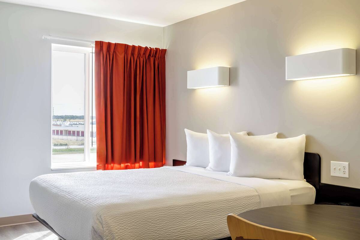A hotel room with a bed, a table, and a window with curtains.