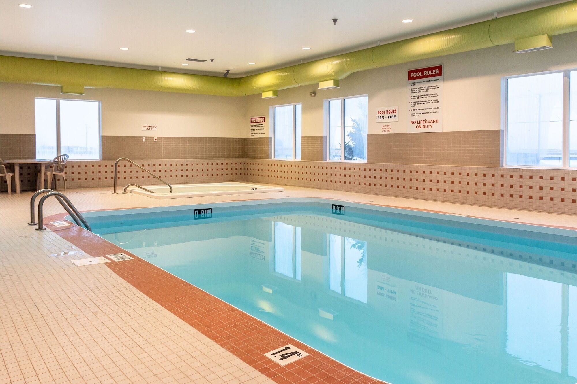 An indoor swimming pool with clear pool rules posted on the wall, including pool hours and no lifeguard on duty.