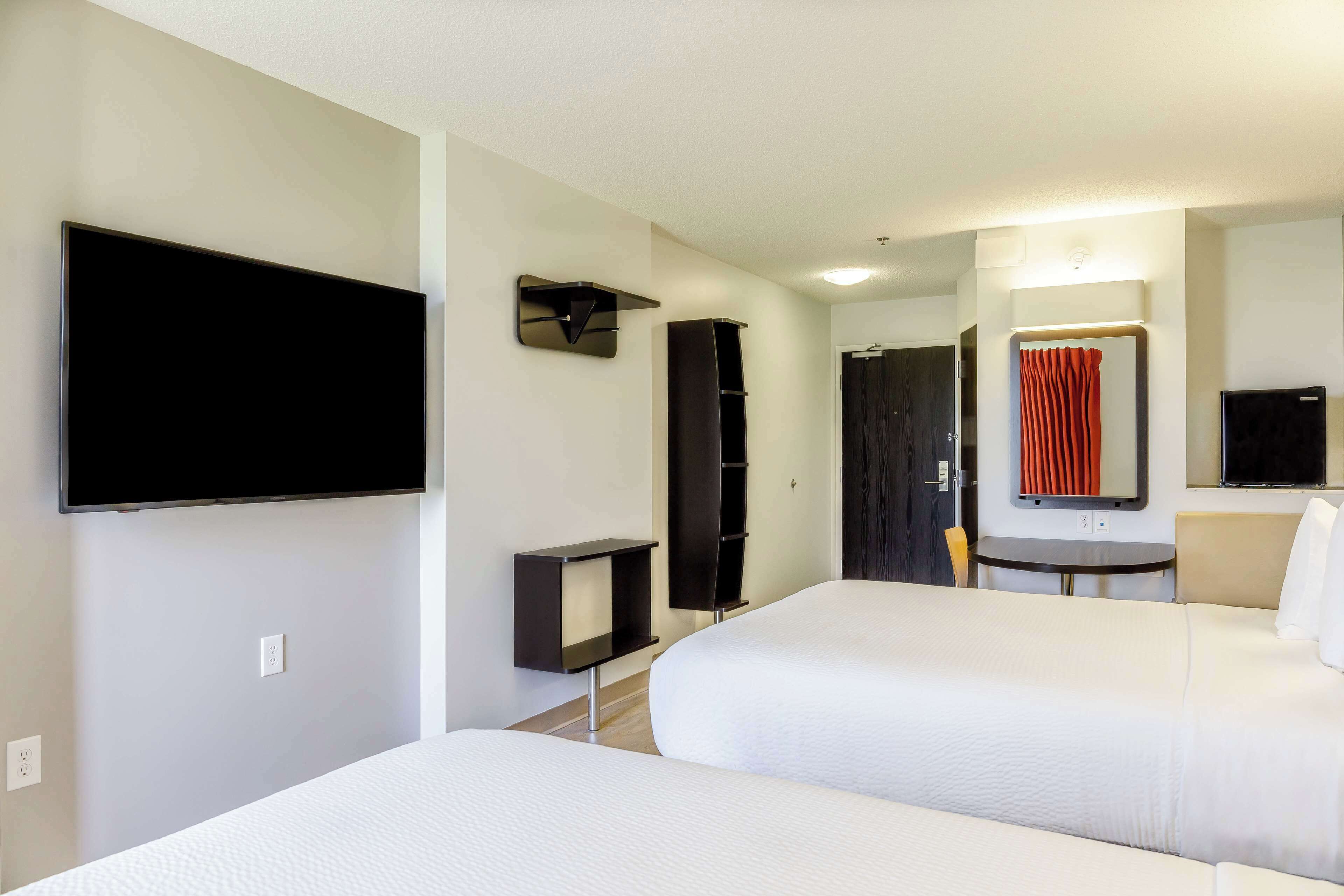 A hotel room with two beds, a flat-screen TV mounted on the wall, a small table, and a mirror.