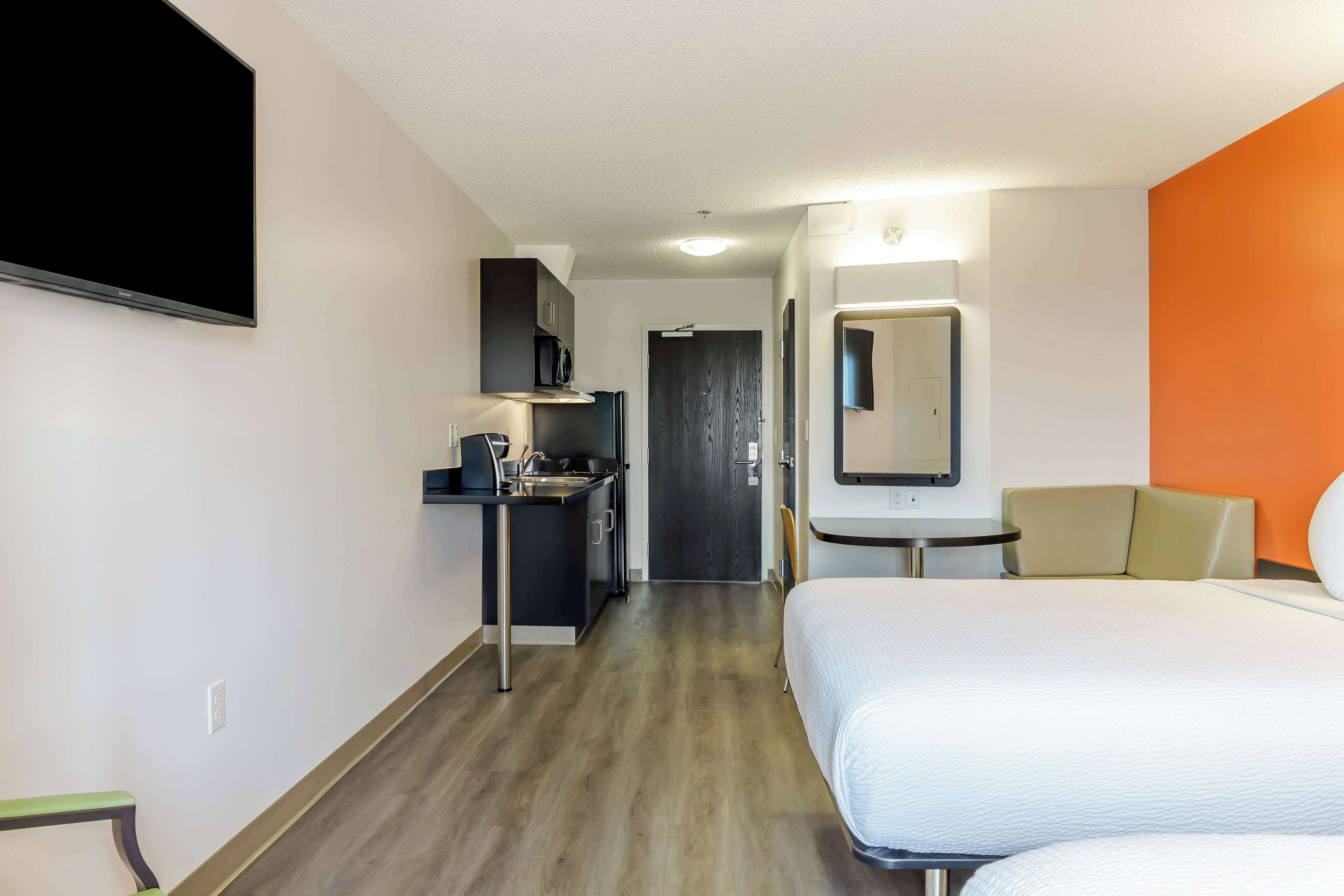 A hotel room with a bed, a desk with a sink, a microwave, and a TV.