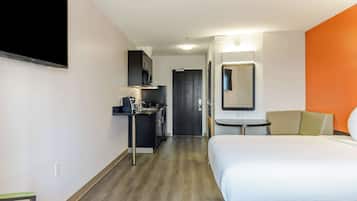 A hotel room with a bed, a desk with a sink, a microwave, and a TV.