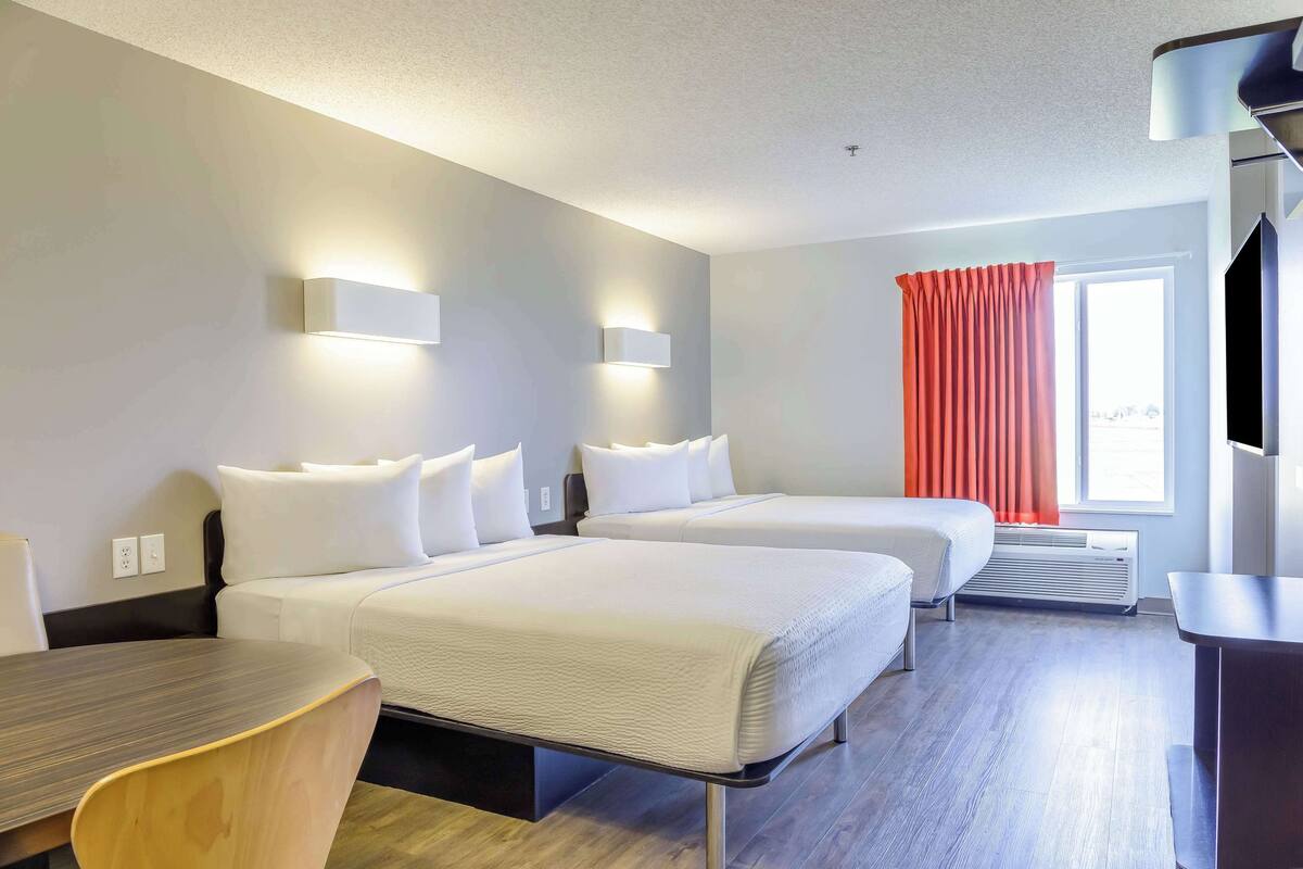 A hotel room with two beds, a desk, and a TV.
