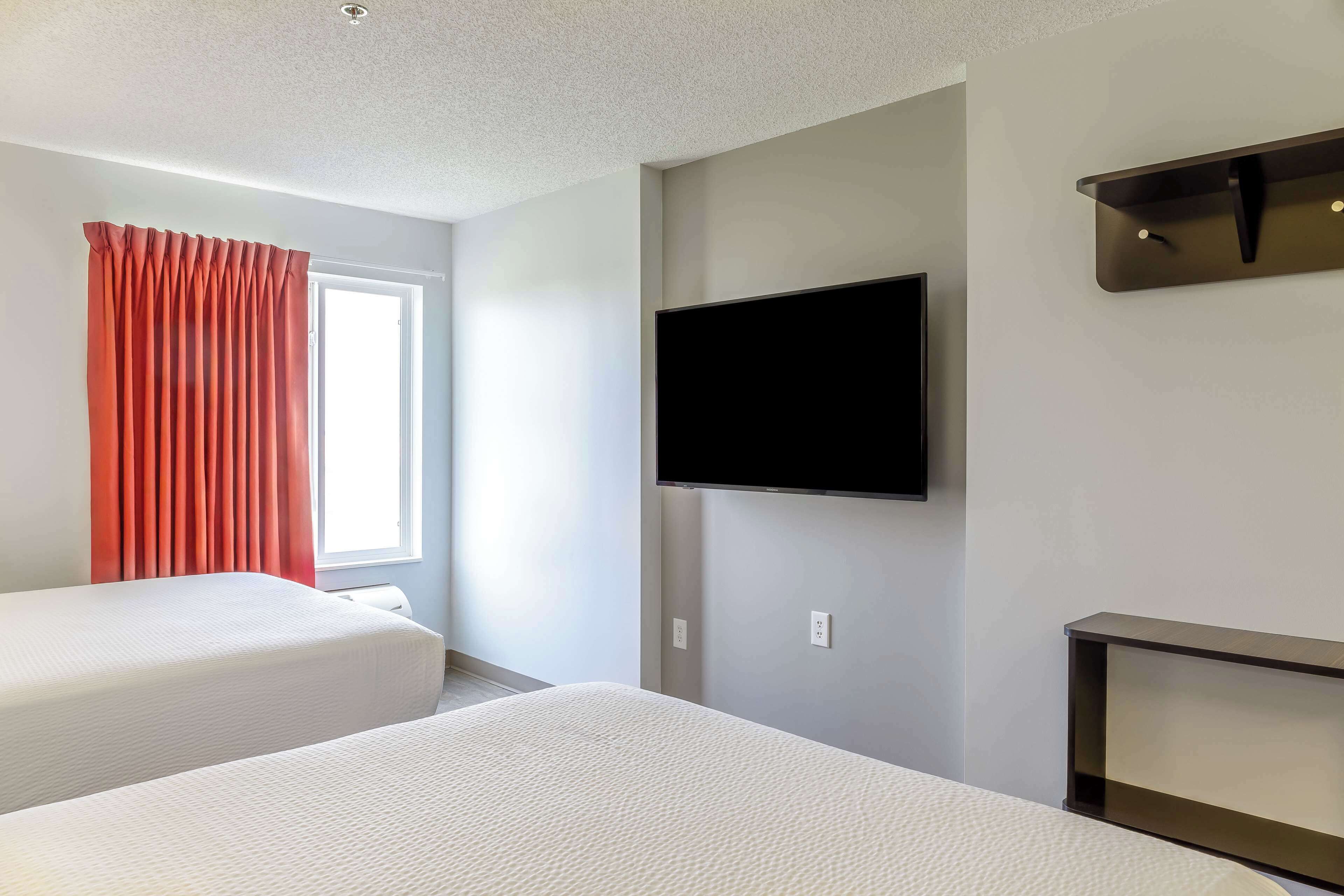 A hotel room with two beds, a flat-screen TV mounted on the wall, and a window with curtains.
