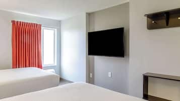 A hotel room with two beds, a flat-screen TV mounted on the wall, and a window with curtains.