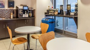 A modern cafe with a coffee machine, trash bin, and seating area. - Motel 6 Headingley, MB - Winnipeg West (Headingley)