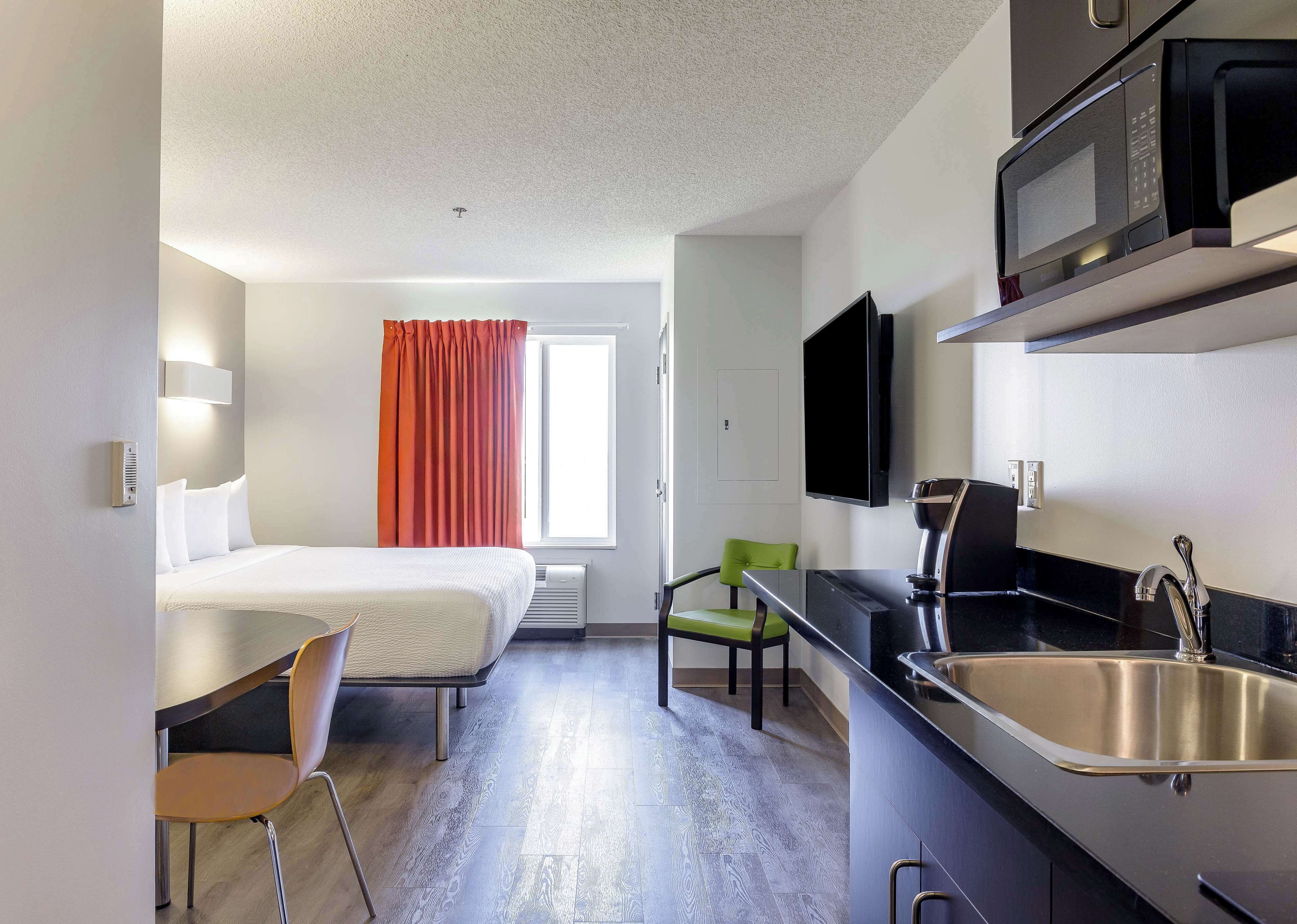 Ein kleines Hotelzimmer mit Bett, einer Küchenzeile, einem Essbereich und einem Fenster mit Vorhängen.