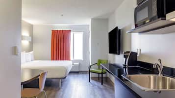 Ein kleines Hotelzimmer mit Bett, einer Küchenzeile, einem Essbereich und einem Fenster mit Vorhängen.