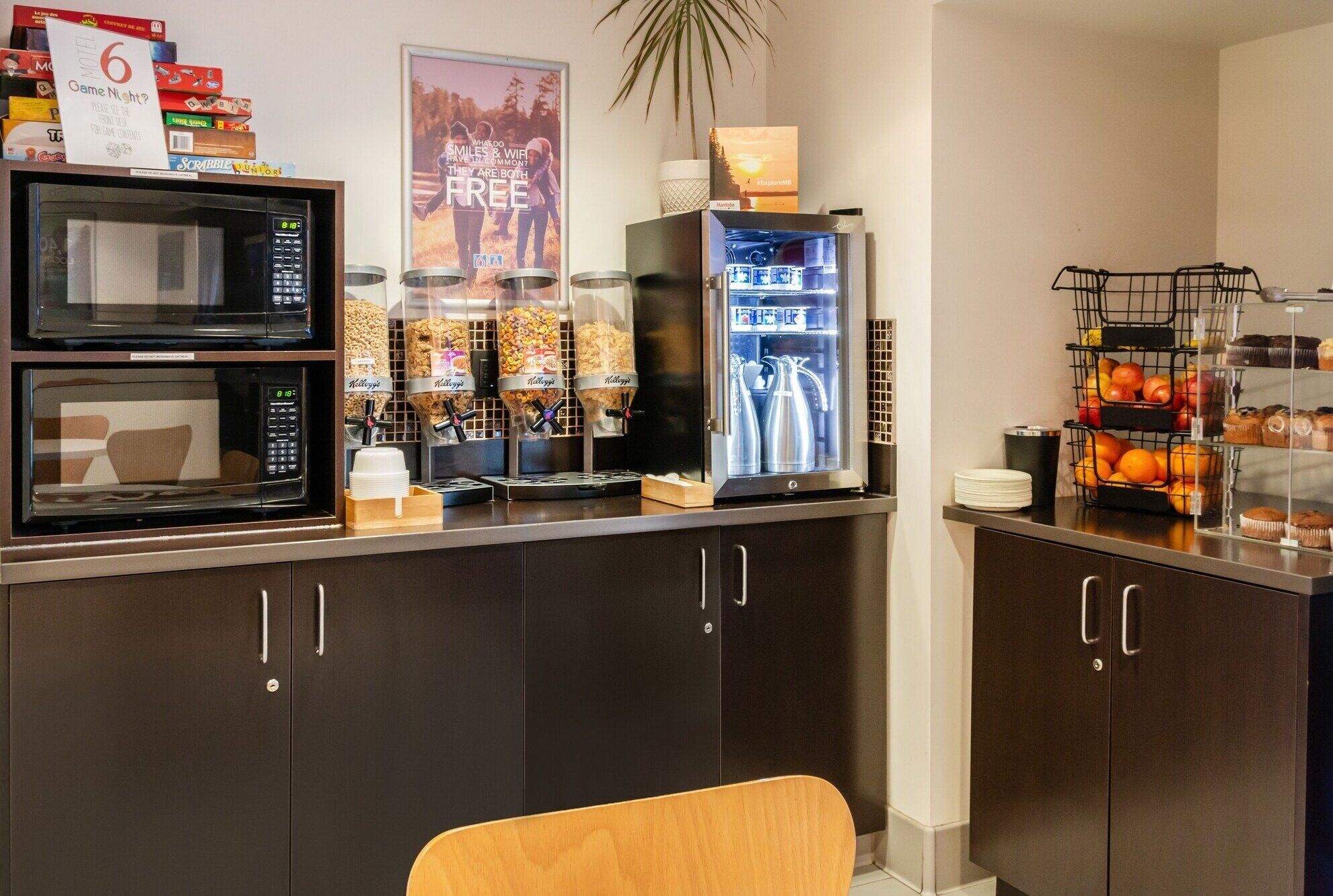 A kitchenette with a microwave, coffee maker, and a refrigerator. There are snack dispensers and a fruit display.