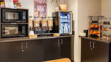A kitchenette with a microwave, coffee maker, and a refrigerator. There are snack dispensers and a fruit display.