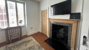 A living room with a fireplace, a television mounted above it, and a window with blinds. - The Barrington Guest House Hotel  (Scarborough)