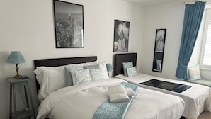 A hotel room with two beds, a nightstand, a lamp, and framed cityscape pictures on the wall. - The Barrington Guest House Hotel  (Scarborough)