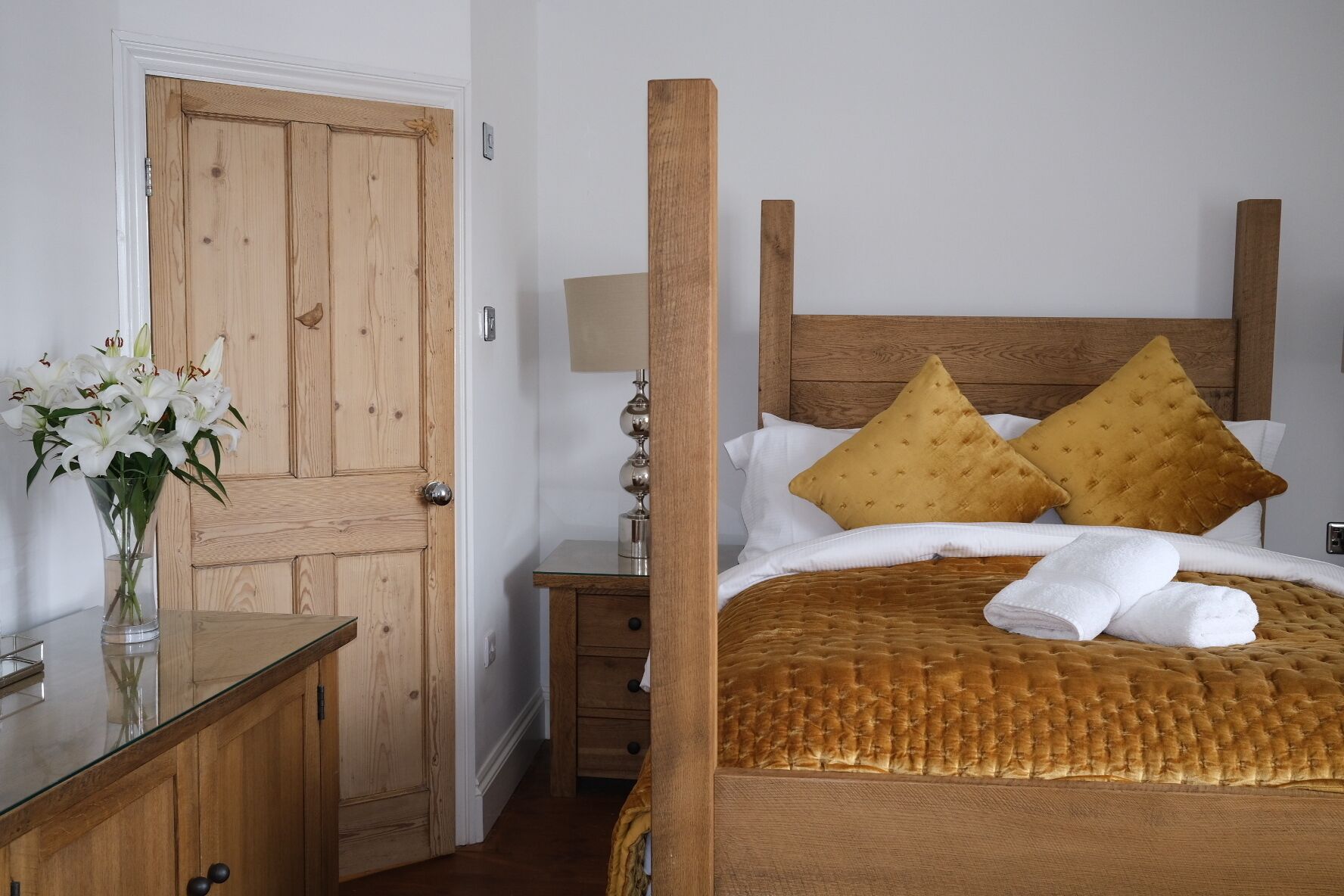 Una cama con dosel de madera con dos almohadas, una mesita de noche y un jarrón con flores.