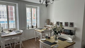 A dining area with a wooden table, white chairs, and a chandelier. There are windows with blinds, a fireplace, and a shelf with decorative items. - The Barrington Guest House Hotel  (Scarborough)