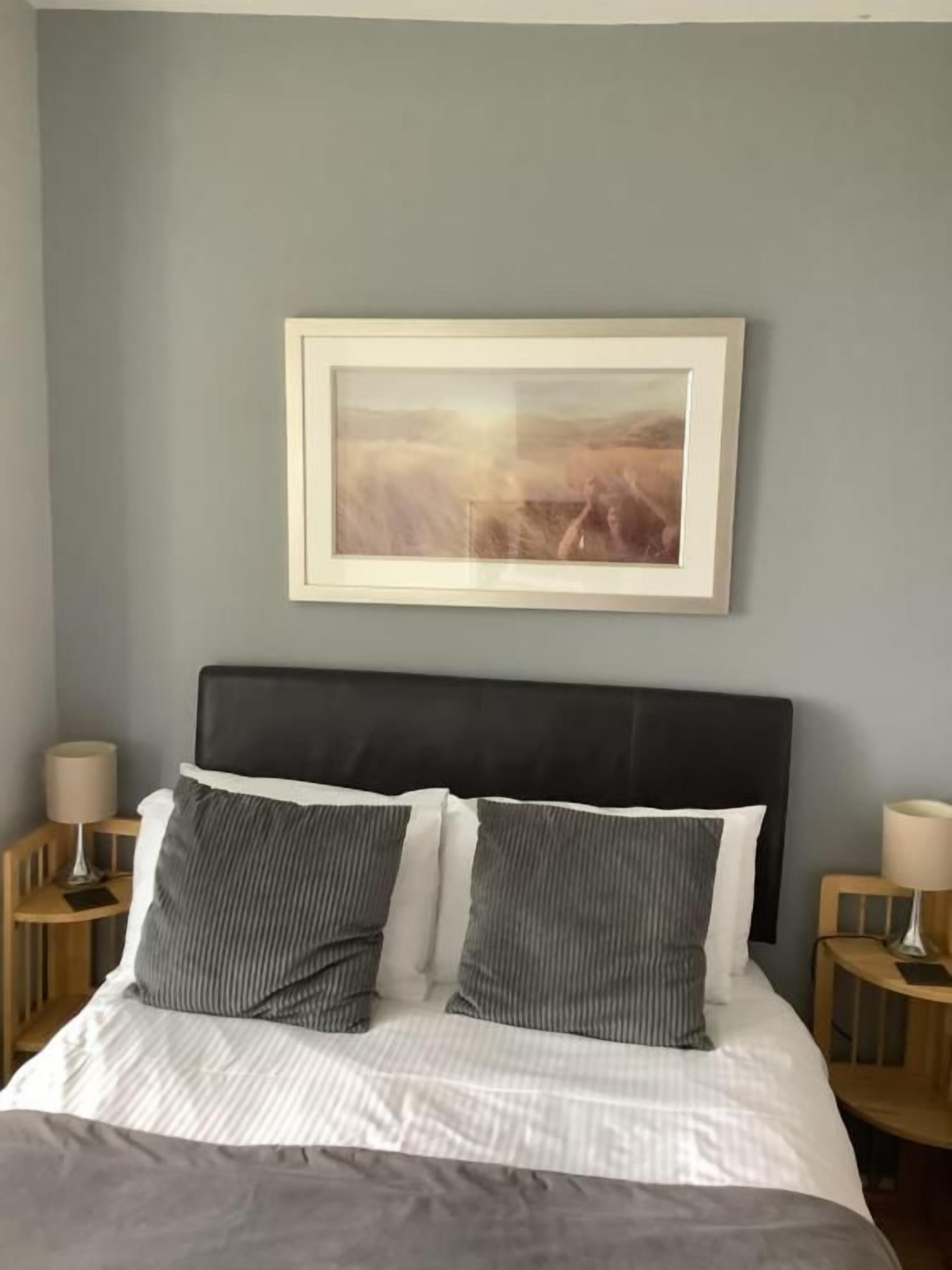 A neatly made bed with a black headboard, two bedside tables with lamps, and a framed picture on the wall.