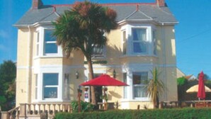 A two-story building with a balcony, a red umbrella, and a palm tree in front. - Beechwood House (St Ives)