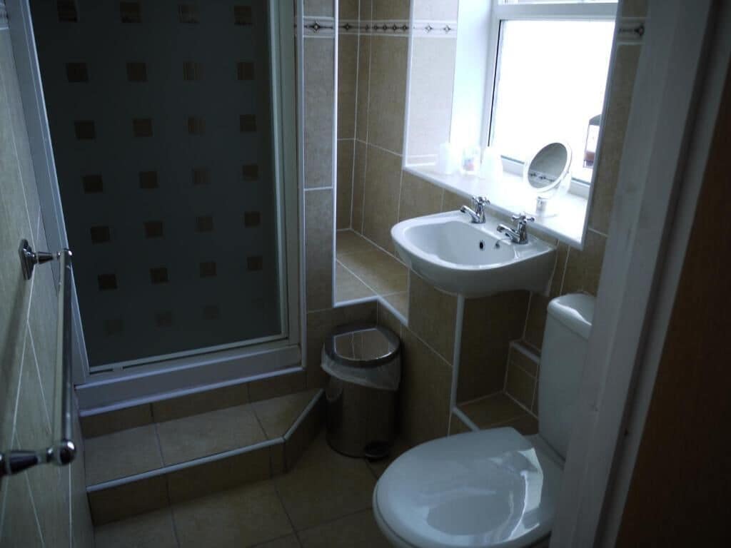 A bathroom with a shower, sink, toilet, and a window.