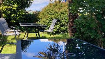 A glass-top table with chairs, surrounded by lush greenery and a palm tree.