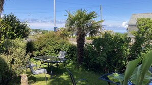 A patio with a table and chairs, surrounded by lush greenery and a palm tree. - Beechwood House (St Ives)