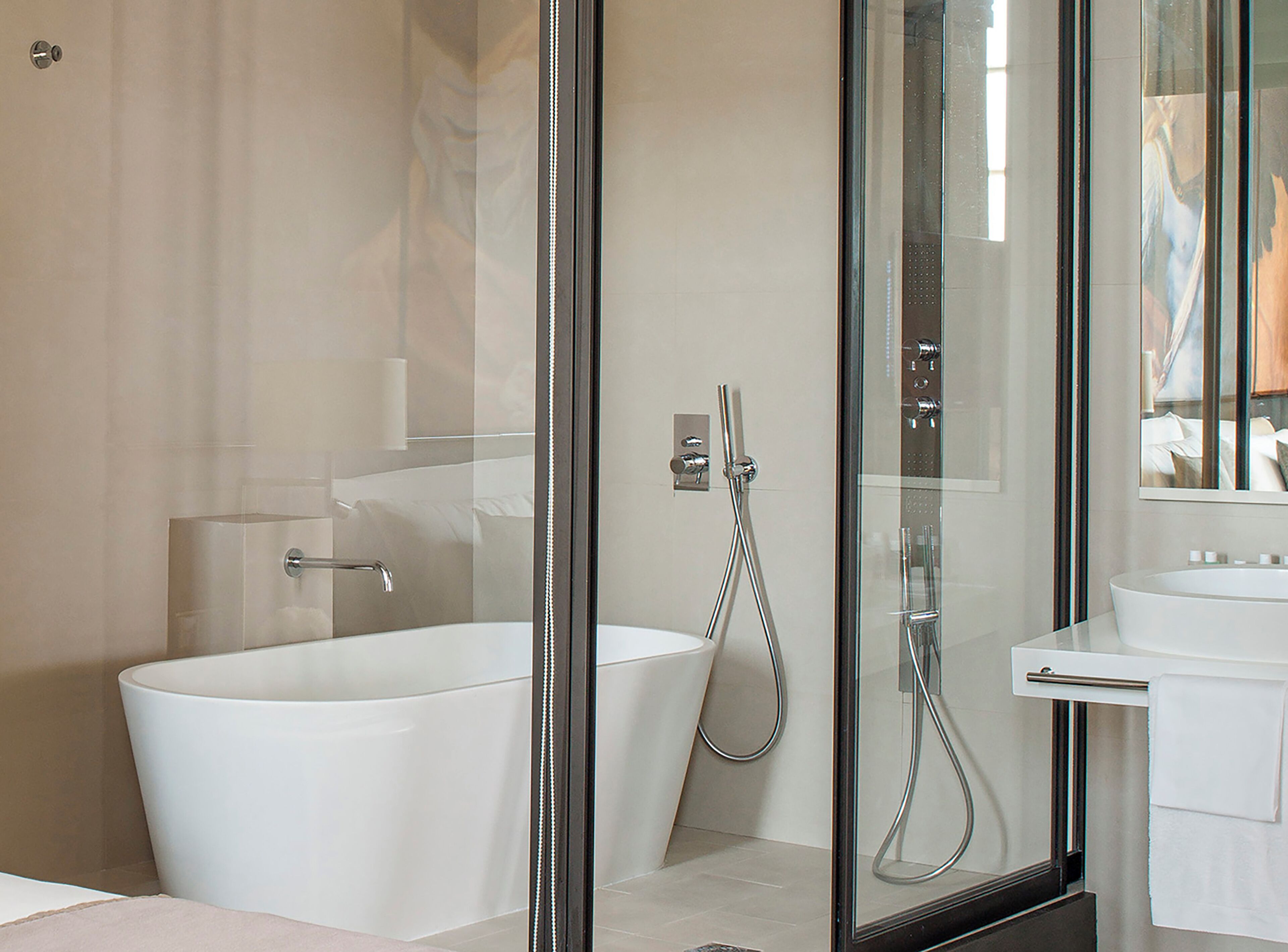 Un baño moderno con una bañera independiente, una zona de ducha con mampara de vidrio y un lavabo blanco.