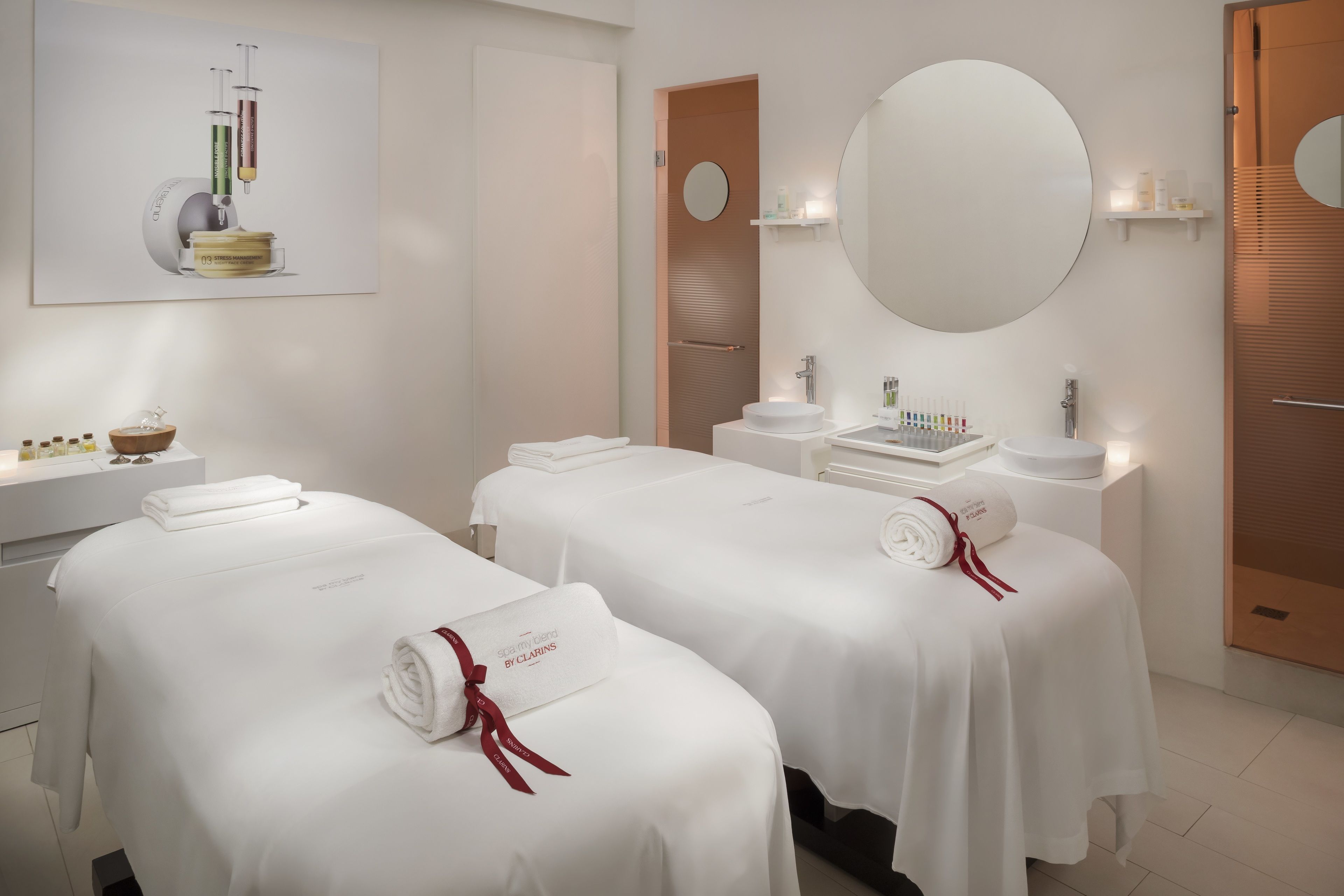 A modern spa room with two treatment beds, a large mirror, and a sink with toiletries.