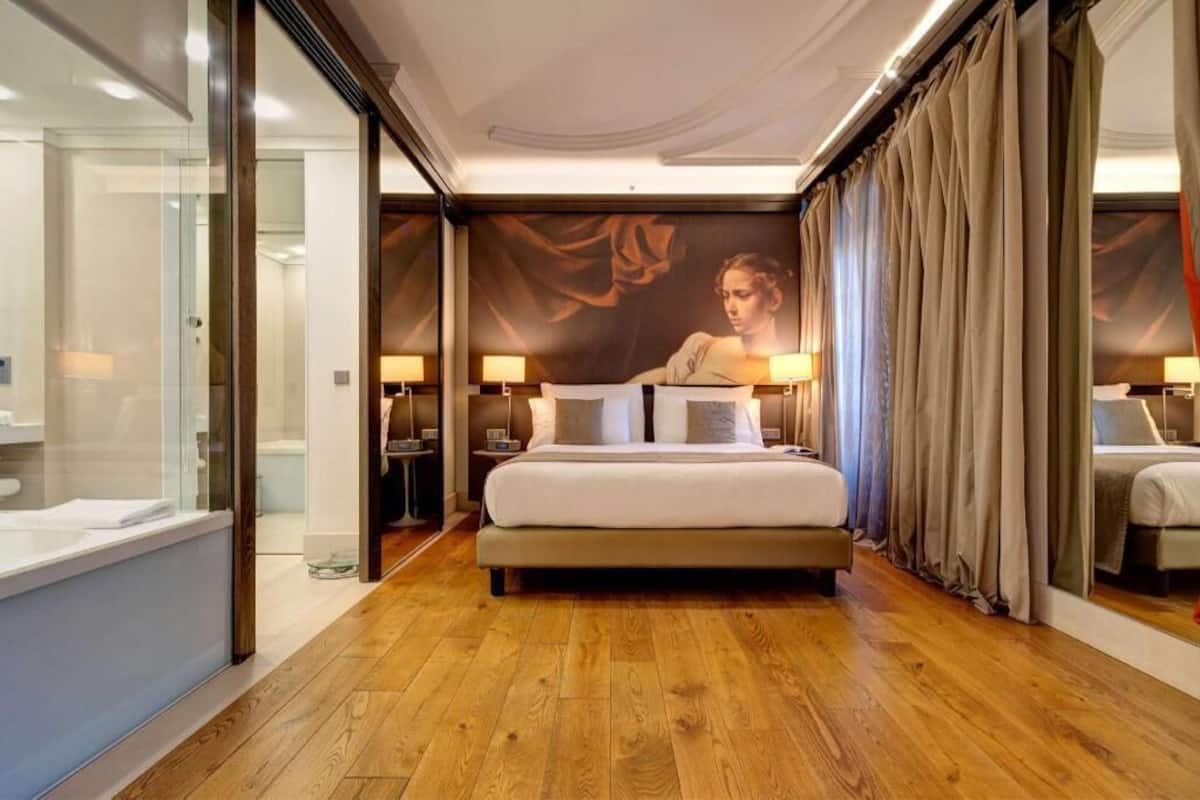 Una camera d'albergo con un letto grande, comodini, box doccia in vetro e un murale sulla parete.