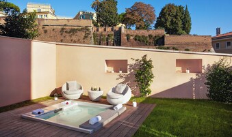 A private outdoor hot tub area with two lounge chairs, a wooden deck, and a brick wall with greenery.
