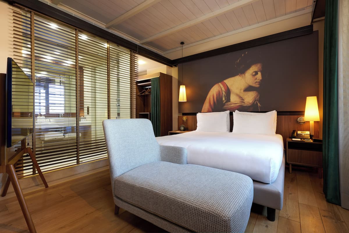 Una camera d'albergo con un letto grande, un'area salotto, un televisore e una finestra con tende.