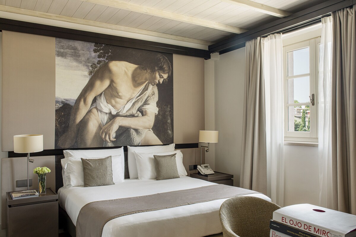 Una habitación de hotel con una cama grande, dos mesitas de noche, una lámpara, una silla y una ventana con cortinas.