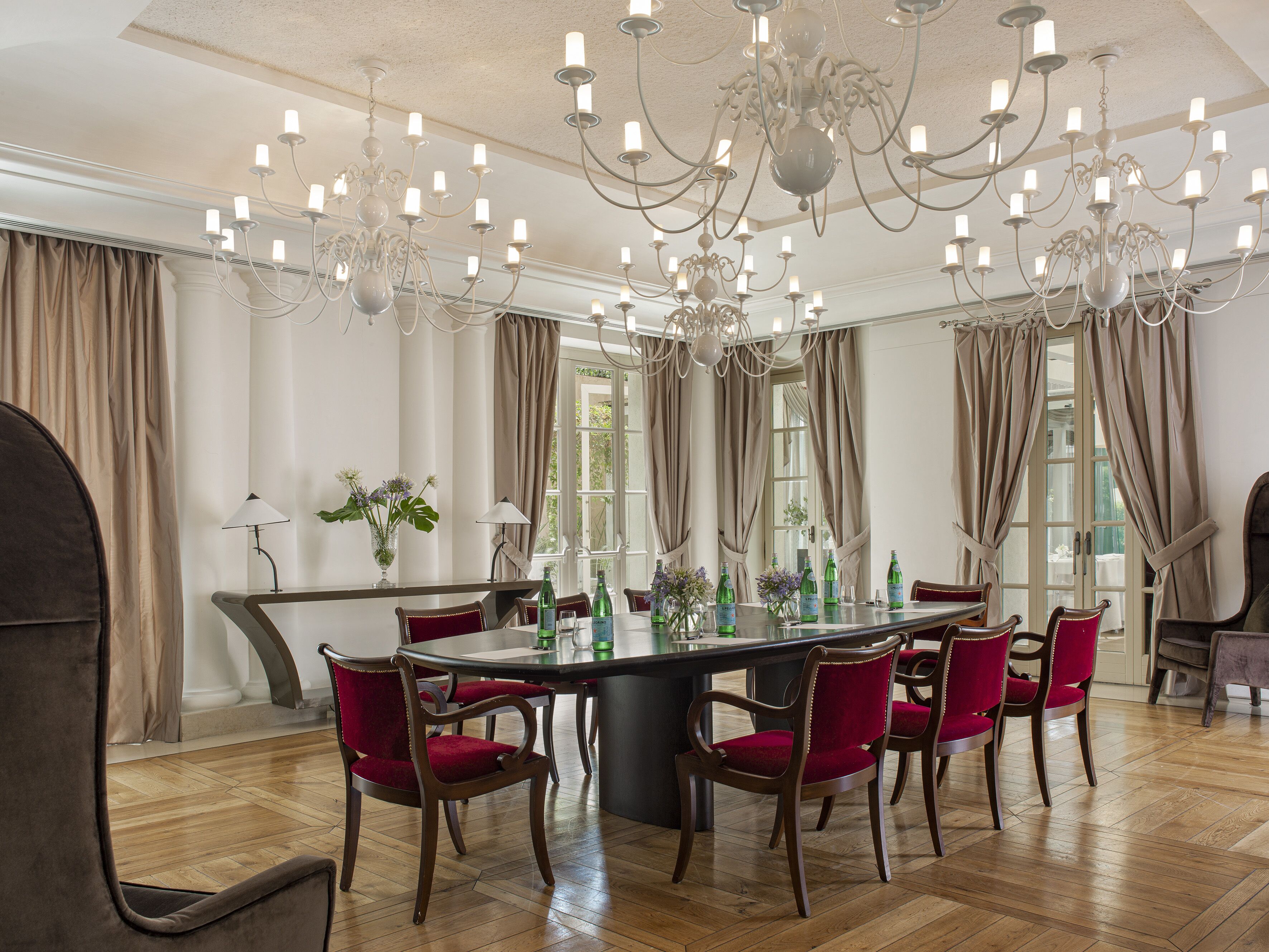 A spacious dining area with a large round table, red upholstered chairs, and a chandelier.