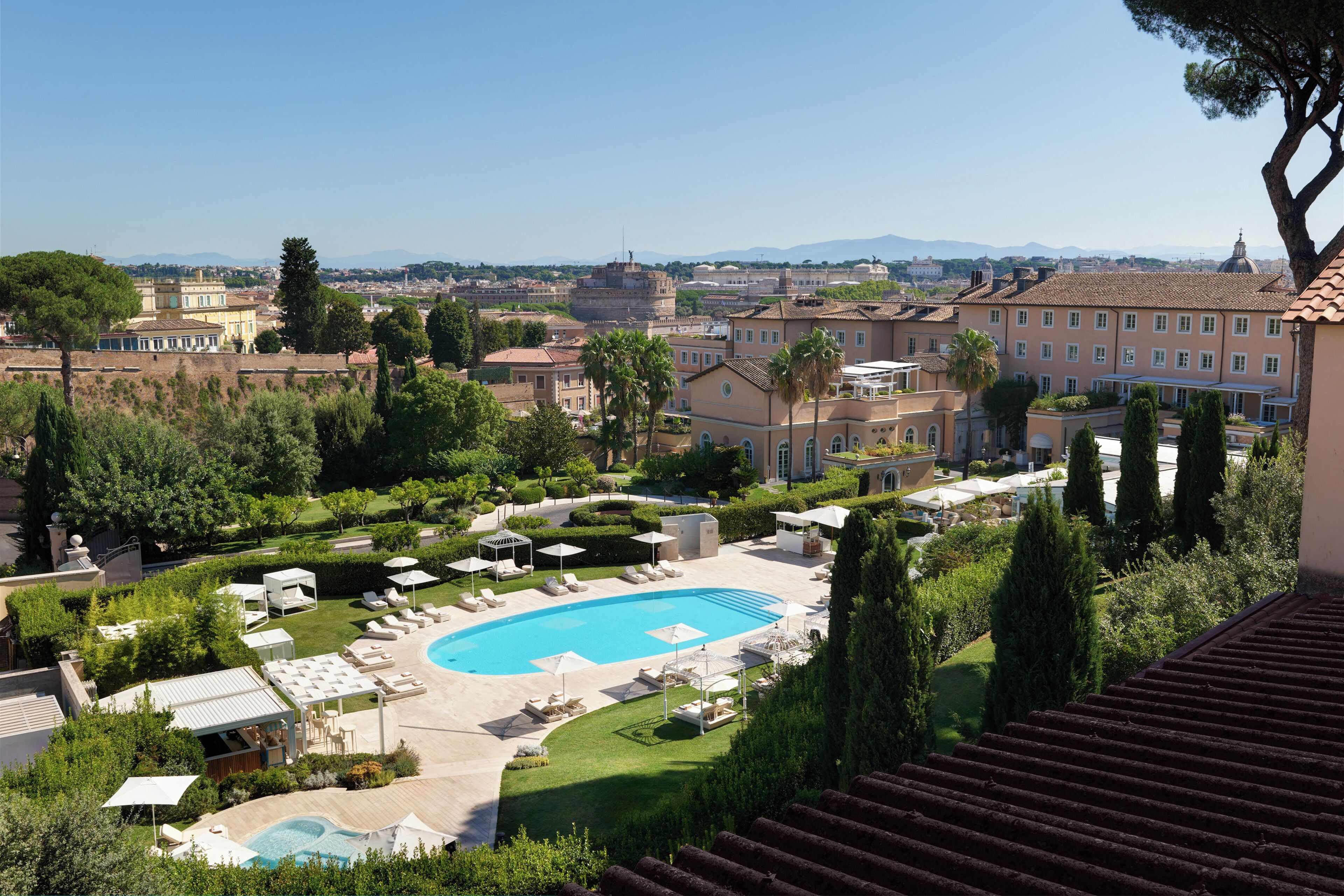 A resort with a large swimming pool, sun loungers, and a view of the surrounding cityscape.