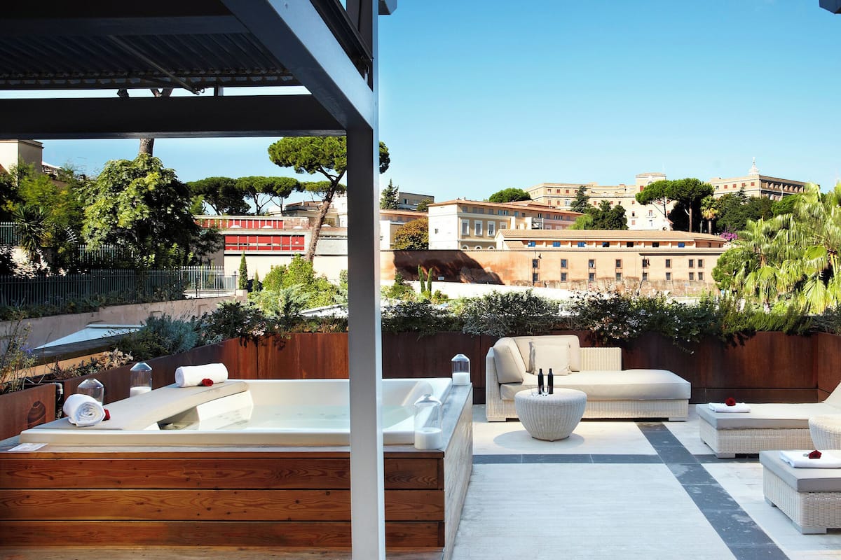 Una terrazza panoramica sul tetto con idromassaggio, poltrone relax e vista su edifici storici.