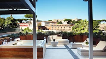 A rooftop terrace with a hot tub, lounge chairs, and a view of historic buildings.