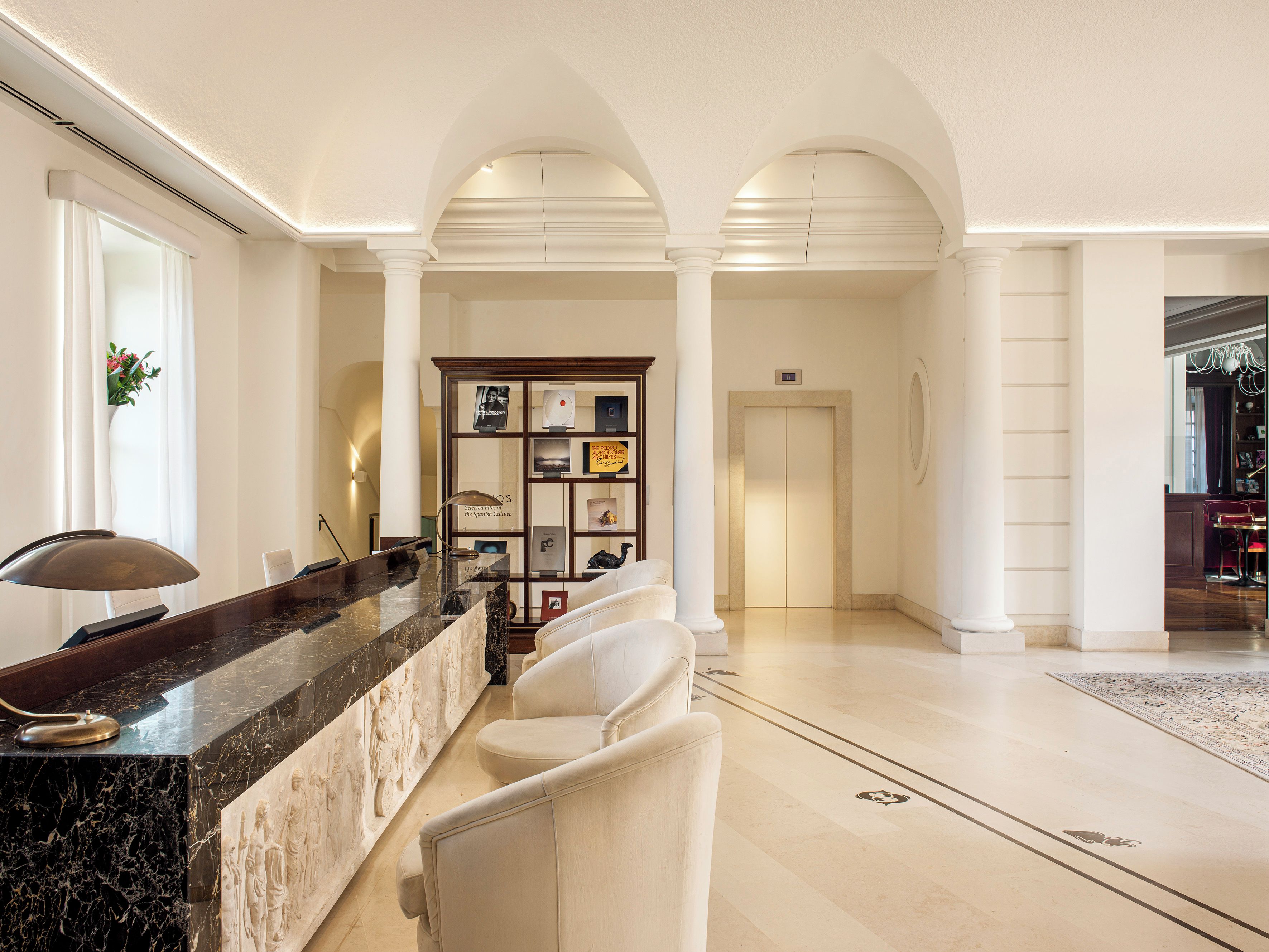 A hotel lobby with a reception desk, seating area, and a bookshelf with various items.