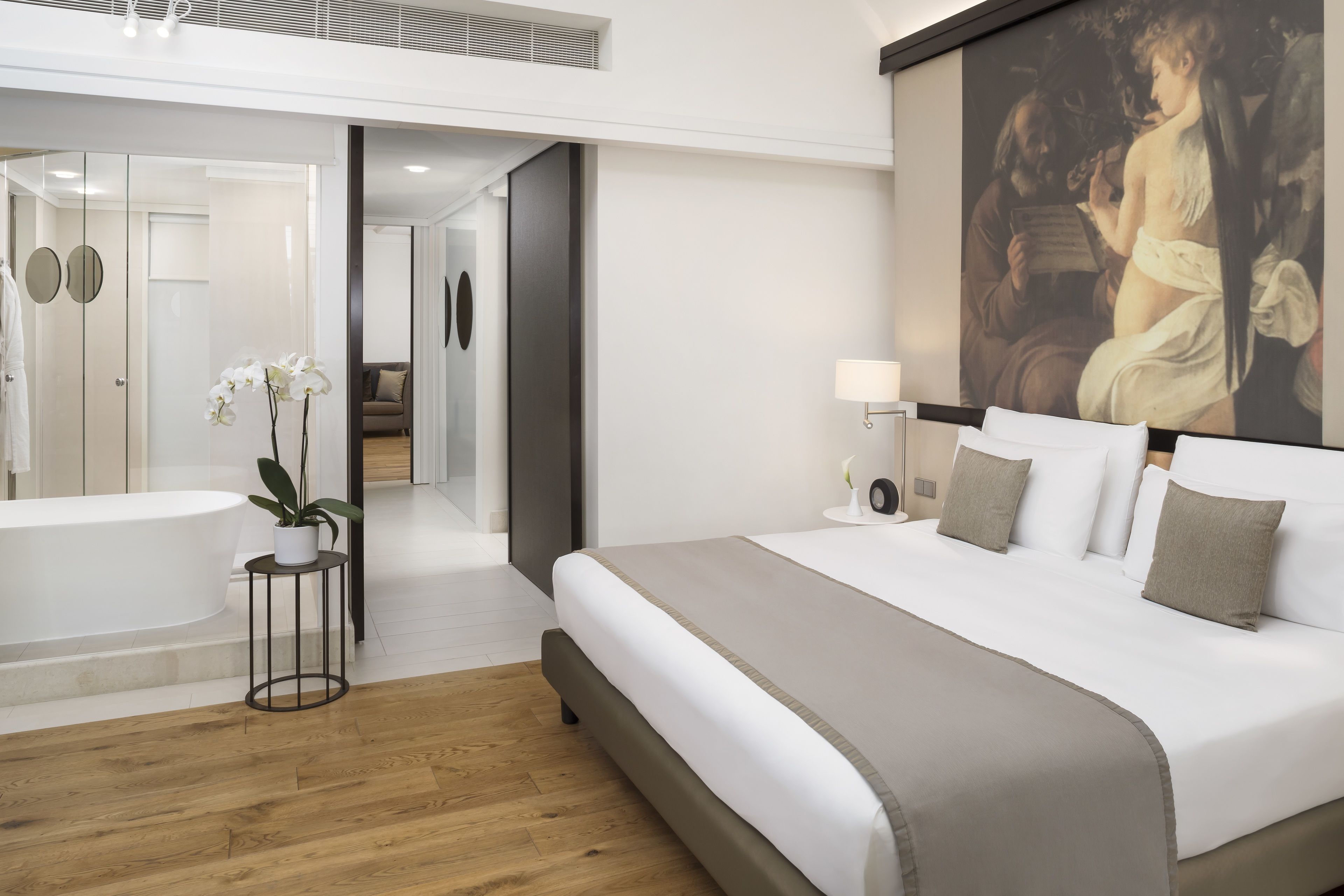 A modern hotel room with a large bed, a bathtub, and a painting on the wall.