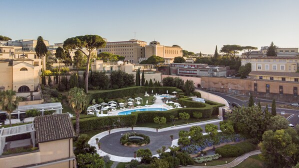 A landscaped garden with a fountain, surrounded by neatly trimmed hedges and palm trees.