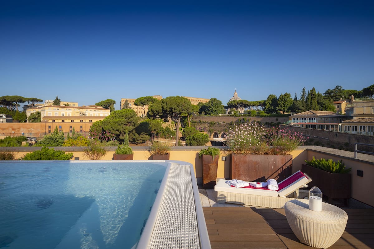 Area piscina sul tetto con vista libera su edifici storici e alberi sullo sfondo.