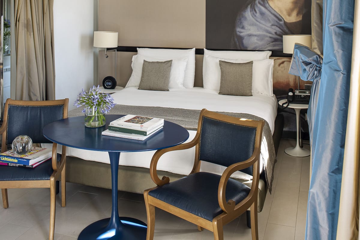Una camera d'albergo con un letto, due poltrone, un tavolo, una lampada e un grande quadro appeso al muro.
