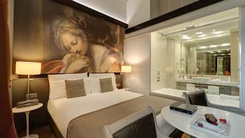 A hotel room with a large bed, bedside lamps, a round table with a book and snacks, and a large mirror above the sink.