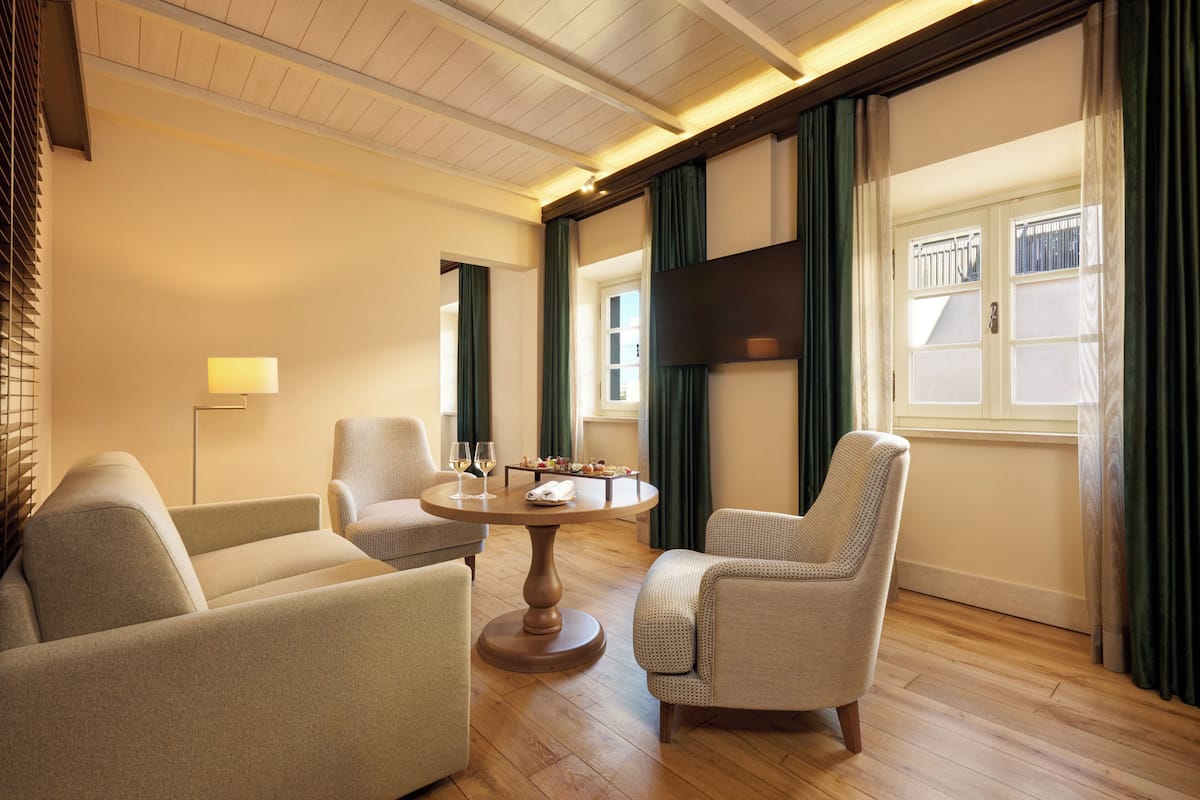 Ein modernes Wohnzimmer mit einem runden Holztisch, zwei Sesseln, einer Stehlampe und einem großen Fernseher an der Wand.
