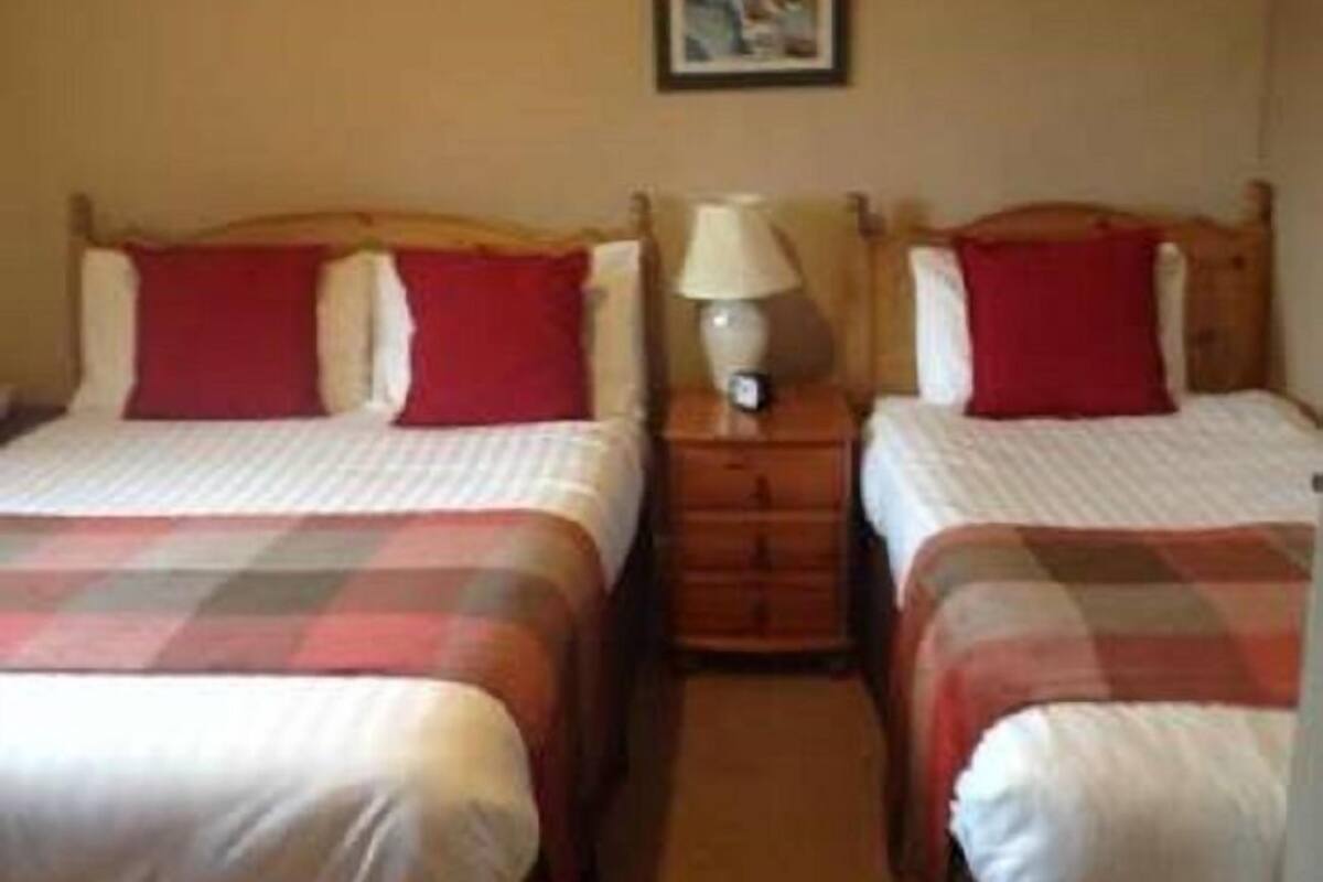 Ett hotellrum med två sängar, var och en med en röd kudde och ett rutigt täcke. Mellan sängarna står ett nattduksbord med en lampa.