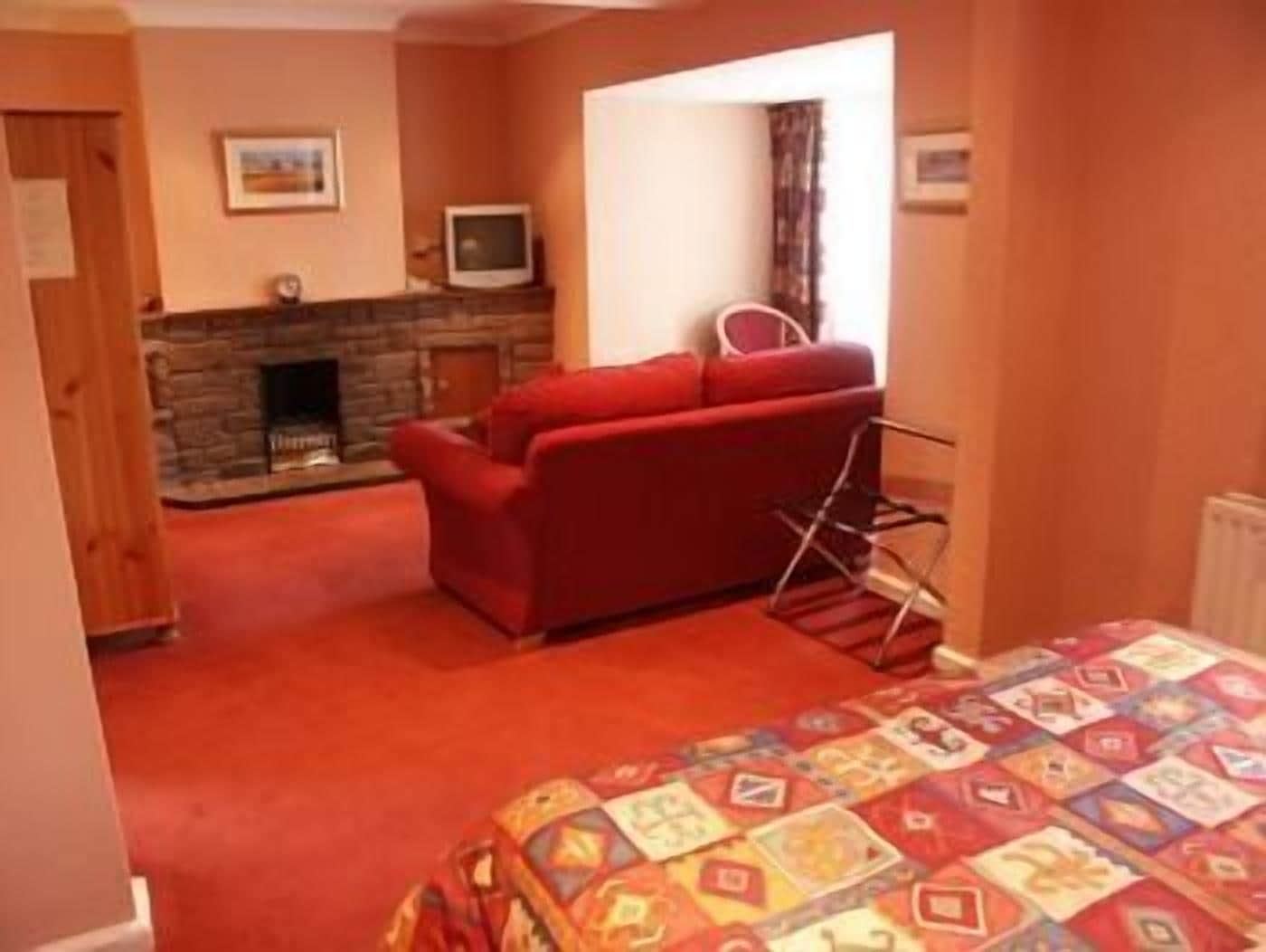 A cozy room with a red sofa, a fireplace, and a patterned bedspread.