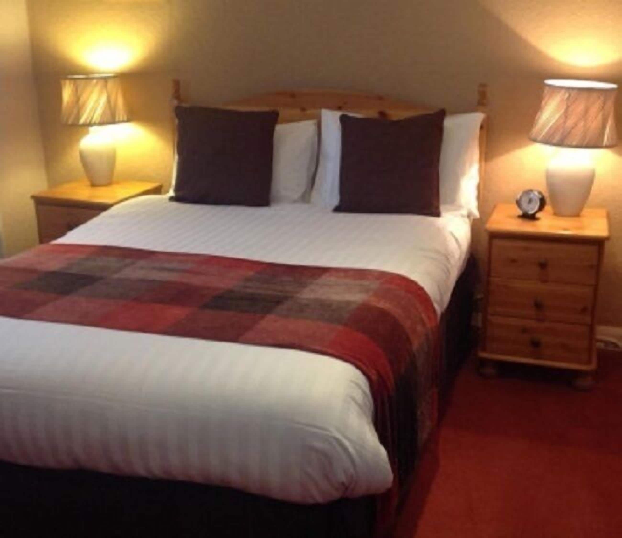 A neatly made bed with a red and white bedspread, two bedside tables with lamps, and a wooden headboard.