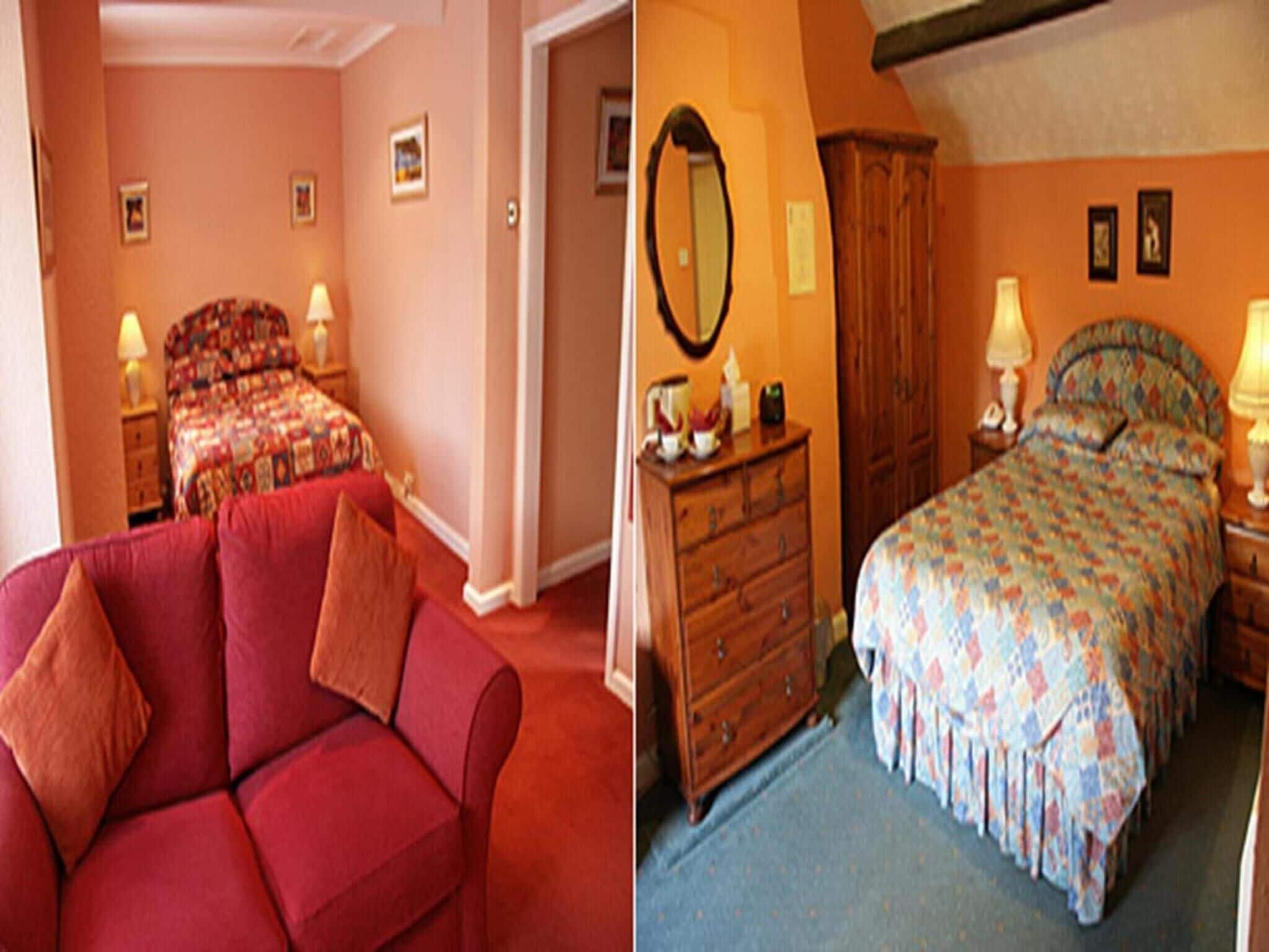 A room with a red sofa, a bed with a floral bedspread, a wooden dresser, and a mirror on the wall.