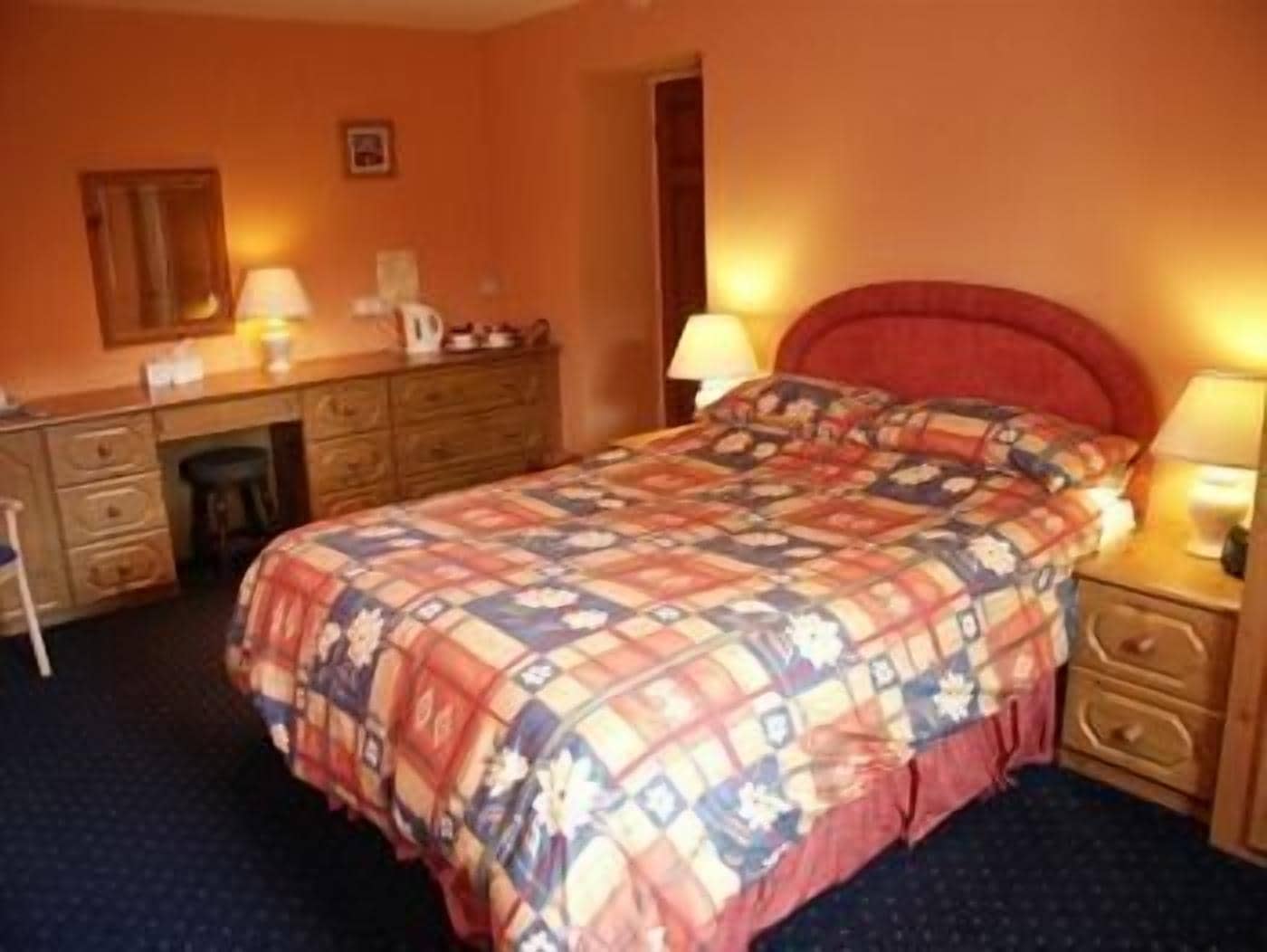 A hotel room with a bed, a desk, a chair, and a dresser.
