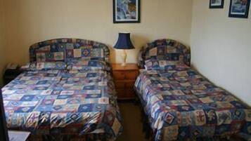 Una habitación con dos camas, cada una con una colcha estampada, una mesita de noche con lámpara y un cuadro en la pared.